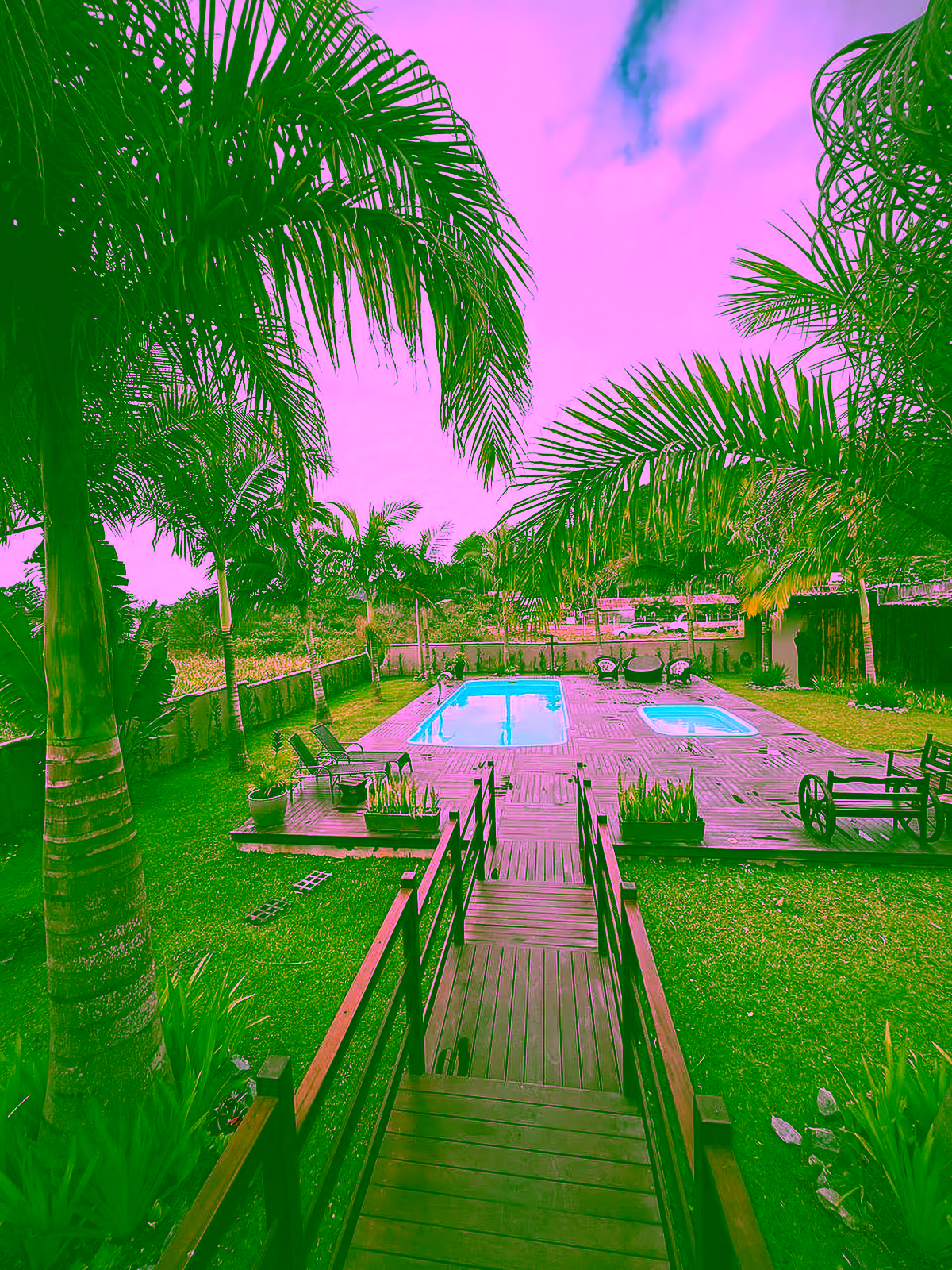 Vista do alto das piscinas, passarela de madeira e jardim do rancho